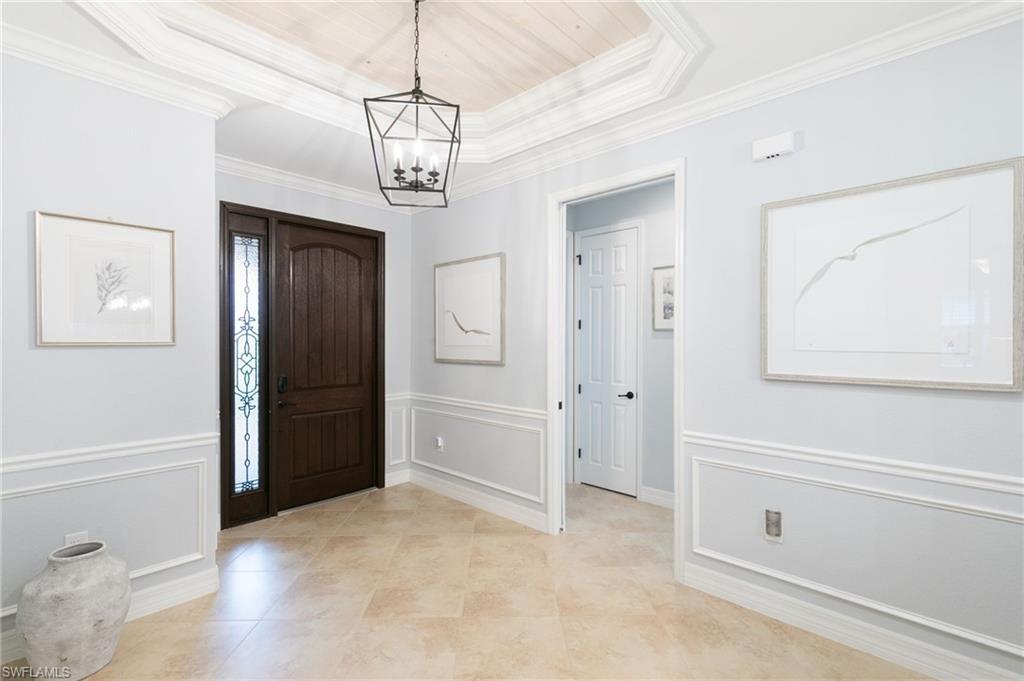 2862 Aviamar Circle Naples, FL 34114 - Photo 4 of 48 Foyer entrance featuring a tray ceiling, light tile patterned flooring, a decorative wall, a chandelier, and crown molding