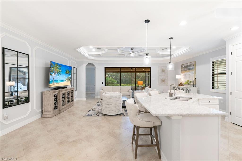 2862 Aviamar Circle Naples, FL 34114 - Photo 8 of 48 Kitchen featuring a raised ceiling, ornamental molding, an island with sink, light stone counters, and decorative light fixtures
