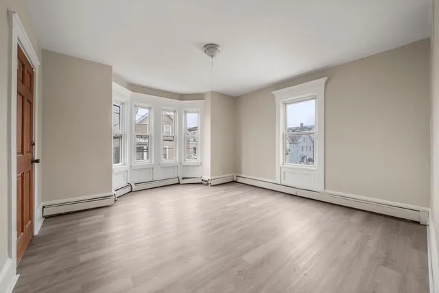 an empty room with wooden floor and windows with curtains