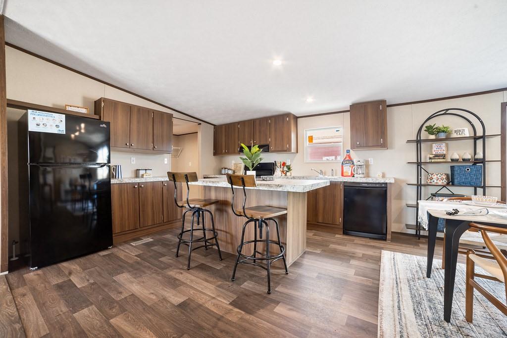 a kitchen with stainless steel appliances kitchen island granite countertop a refrigerator a stove a sink dishwasher and a dining table with wooden floor