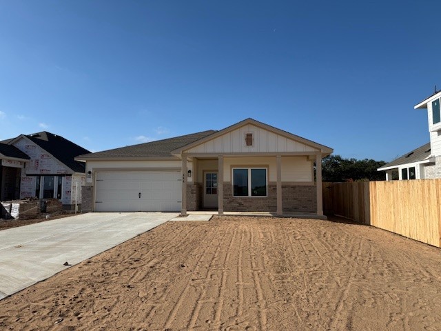 Ranch-style house with concrete driveway, brick siding, covered porch, board and batten siding, and a garage