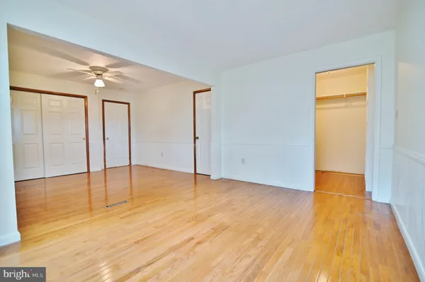 an empty room with wooden floor fan and windows