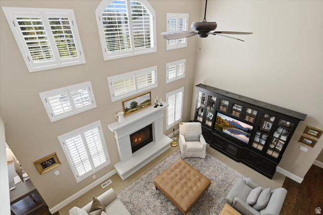 1257 Rigby Road Kaysville, UT 84037 - Photo 30 of 55 Two-story living area featuring a central fireplace with a substantial mantel, multiple windows with white plantation shutters, a ceiling fan, and hardwood flooring visible in the entry