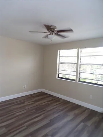 an empty room with wooden floor ceiling fan and windows