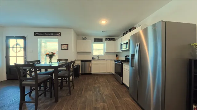 a kitchen with stainless steel appliances a dining table chairs refrigerator and window