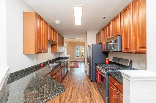 a kitchen with stainless steel appliances granite countertop a refrigerator a stove top oven and wooden floors