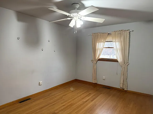 an empty room with wooden floor chandelier fan and windows