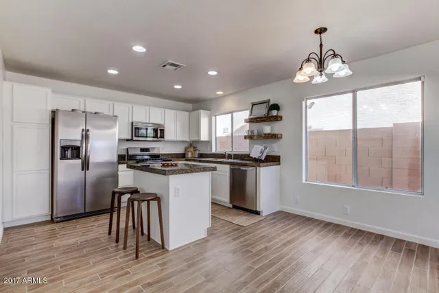 a kitchen with granite countertop a refrigerator a sink dishwasher a stove and white cabinets with wooden floor