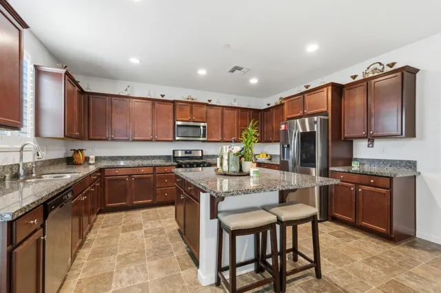 a kitchen with kitchen island granite countertop wooden cabinets a stove a sink a oven with a dining table and chairs