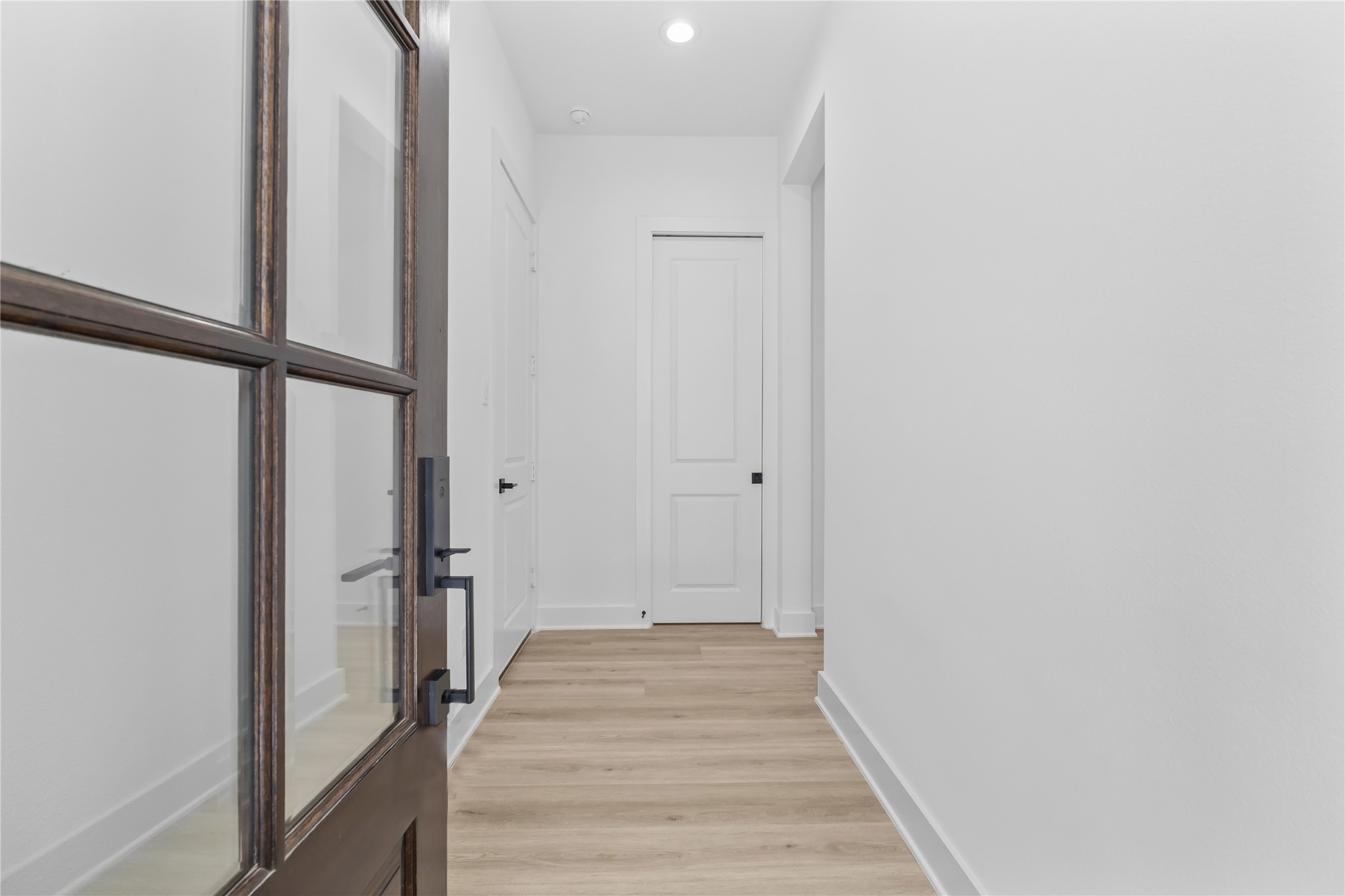 3426 Bolin Road Houston, TX 77092 - Photo 2 of 34 This is a sleek, modern hallway featuring light wood flooring, crisp white walls, and a series of white doors, offering a clean and minimalistic aesthetic. A glass-paneled door adds an elegant touch to the space.