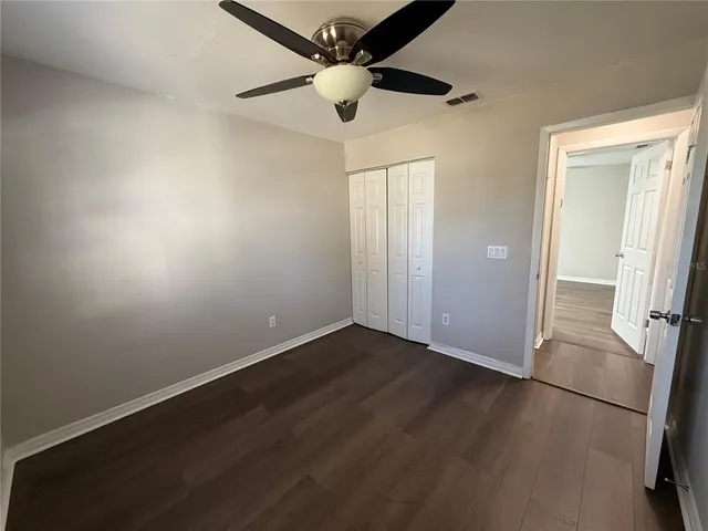 an empty room with wooden floor fan and windows