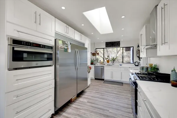 a kitchen with stainless steel appliances granite countertop a stove top oven a sink dishwasher and a refrigerator with wooden floor