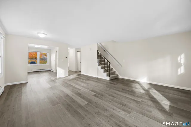 a view of an empty room with wooden floor and stairs