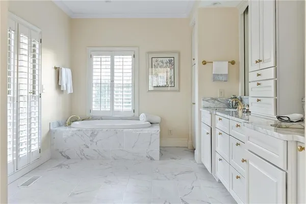 a spacious en suite bathroom with a granite countertop double vanity sink a mirror and a bathtub