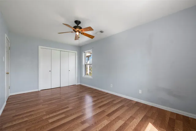 a view of an empty room with wooden floor and a ceiling fan