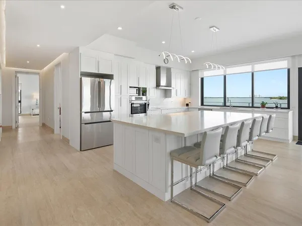 a large white kitchen with kitchen island a large window a sink and cabinets