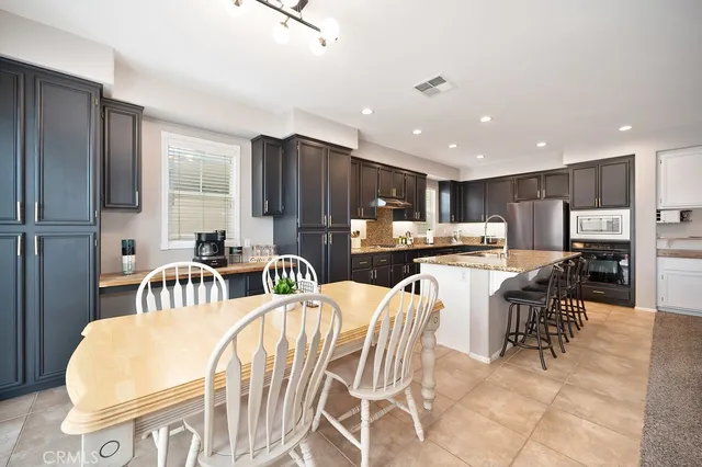 a kitchen with stainless steel appliances kitchen island granite countertop a refrigerator a stove a sink a dining table and chairs with wooden floor