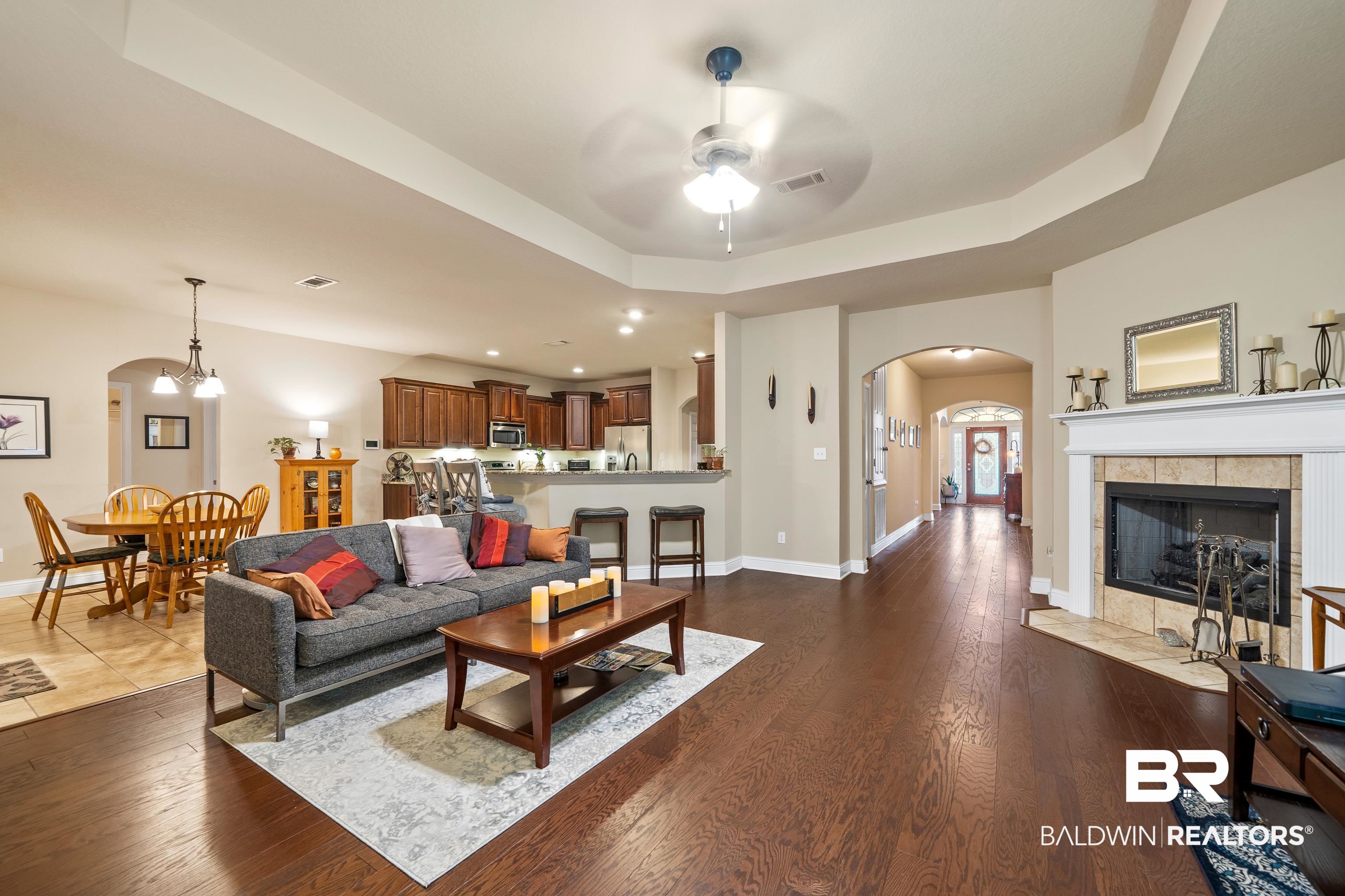 9115 Krystal Ridge Court Daphne, AL 36526 - Photo 9 of 39 Living room featuring a tile fireplace, a raised ceiling, ceiling fan, and dark wood-type flooring