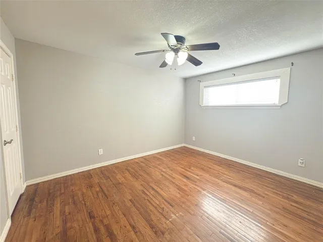 an empty room with wooden floor fan and windows