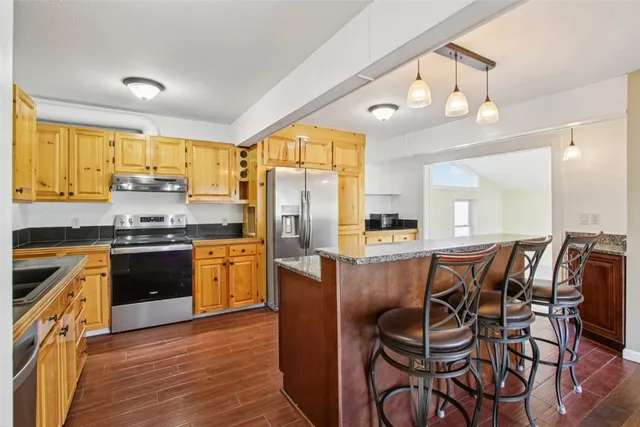 a kitchen with stainless steel appliances granite countertop a stove top oven a refrigerator a sink and dining table with wooden floor