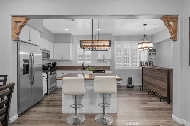 a kitchen with stainless steel appliances a stove a refrigerator a sink a dining table and chairs with wooden floor