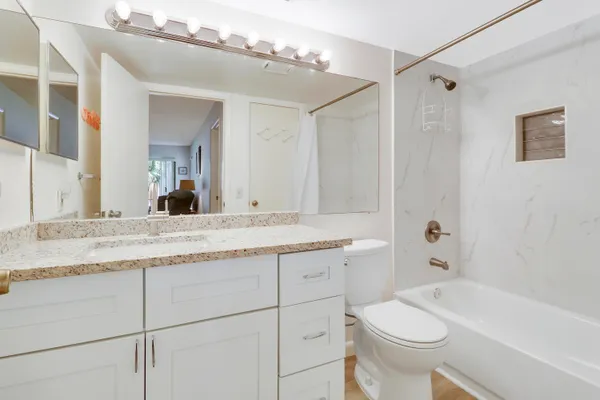 a bathroom with a granite countertop sink a toilet a mirror a vanity and bathtub