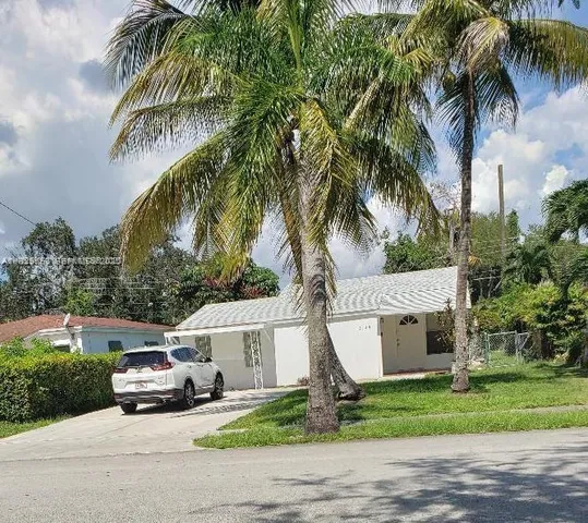 a car parked in front of yellow house with a small yard and palm trees
