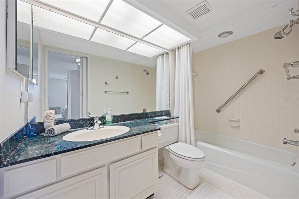 9425 Blind Pass Road, Unit 1006 St. Pete Beach, FL 33706 - Photo 23 of 45 a bathroom with a granite countertop sink toilet a large mirror and shower