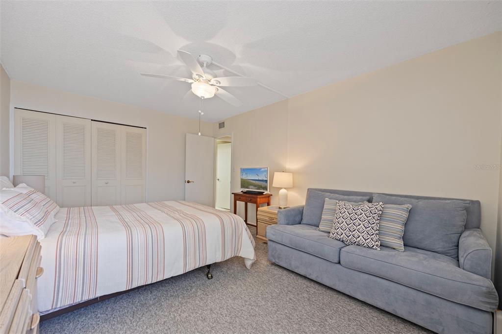 9425 Blind Pass Road, Unit 1006 St. Pete Beach, FL 33706 - Photo 28 of 45 a bedroom with a large bed couch and a ceiling fan