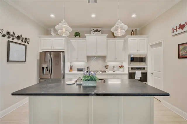 a kitchen with kitchen island granite countertop stainless steel appliances a refrigerator a stove a sink dishwasher and white cabinets with wooden floor