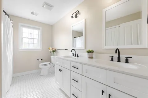 a bathroom with double sink a toilet and a window