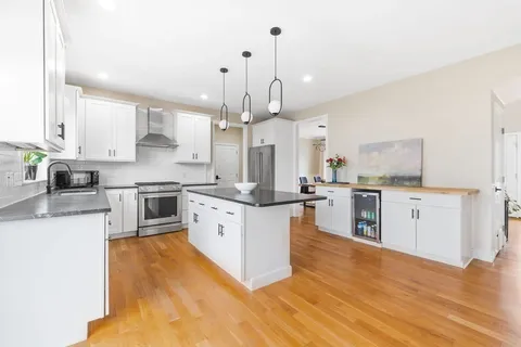 a large kitchen with stainless steel appliances kitchen island granite countertop a stove a sink a refrigerator and white cabinets with wooden floor
