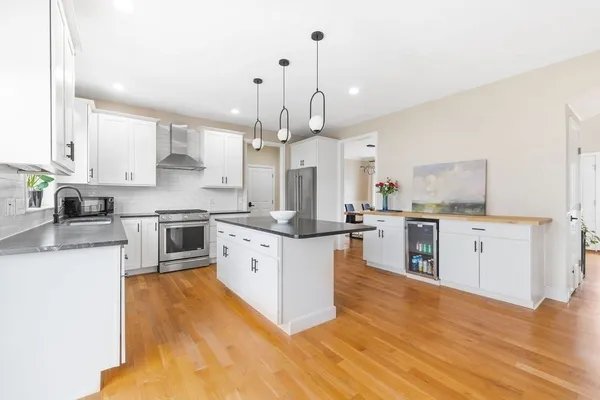 a large kitchen with stainless steel appliances kitchen island granite countertop a stove a sink a refrigerator and white cabinets with wooden floor