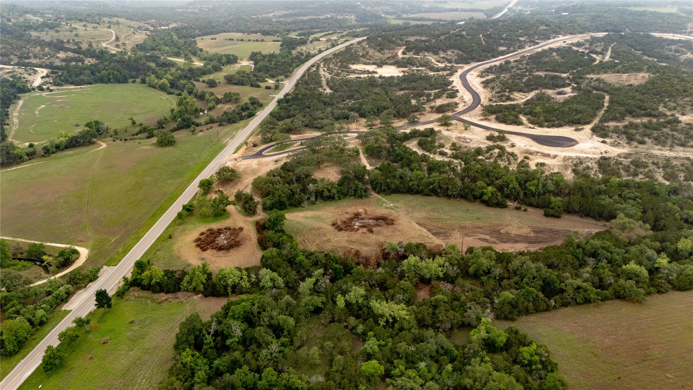 Lot 26 Ranch Road 165 Dripping Springs, TX 78620 - Photo 7 of 13 Expansive undeveloped land featuring a paved road, natural tree coverage, open grassy areas, and new road construction