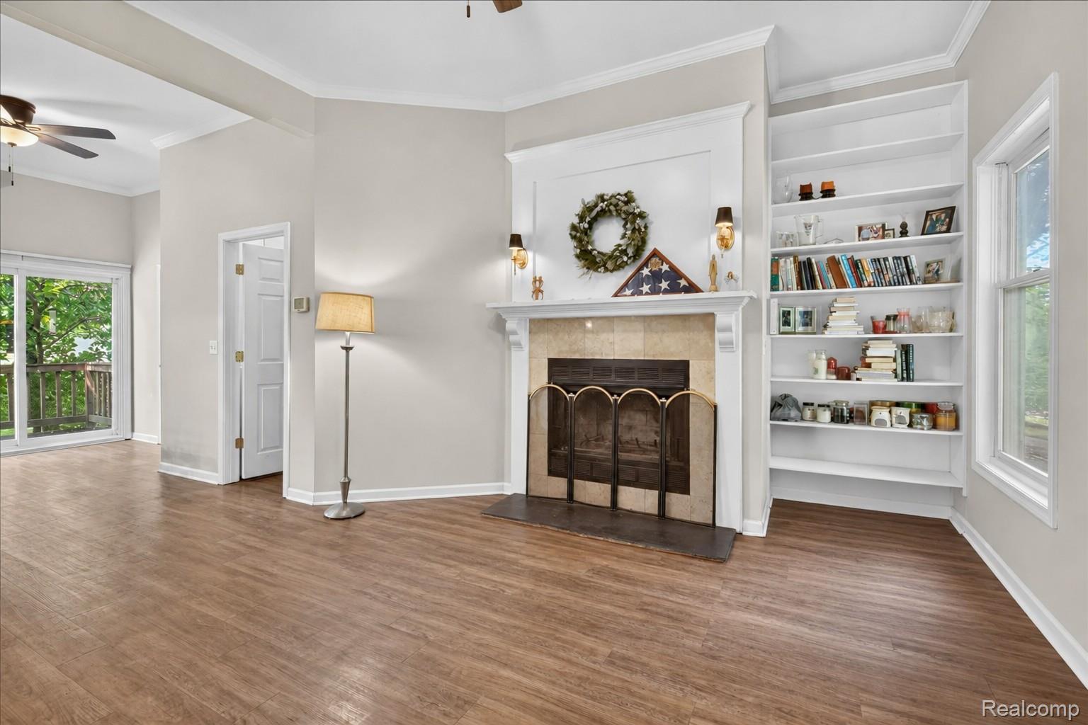 8114 Chilson Road Pinckney, MI 48169 - Photo 17 of 32 Living area featuring a fireplace with a tile surround and white mantel, built-in shelving, wood-finish flooring, and a sliding glass door to an outdoor deck