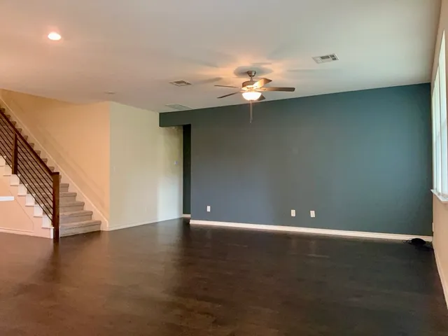 a view of an empty room with wooden floor and a ceiling fan