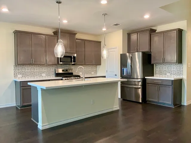 a kitchen with stainless steel appliances granite countertop a refrigerator a sink dishwasher a stove and a oven with wooden floor