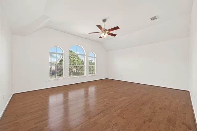 an empty room with wooden floor fan and windows