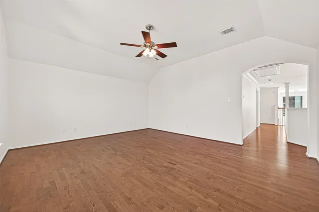 an empty room with wooden floor a ceiling fan and windows