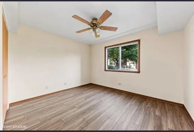 an empty room with wooden floor windows and fan
