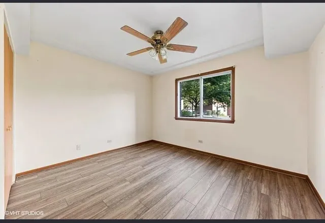 an empty room with wooden floor windows and fan