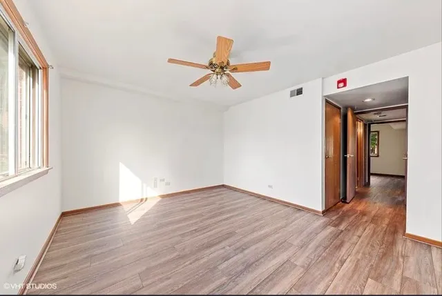 an empty room with wooden floor ceiling fan and windows