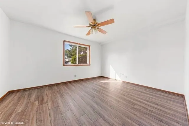 an empty room with wooden floor a ceiling fan and windows