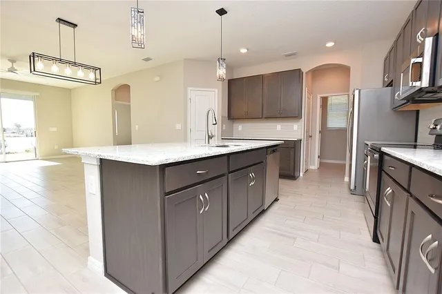 a large kitchen with stainless steel appliances kitchen island a large counter top a sink a stove and a refrigerator