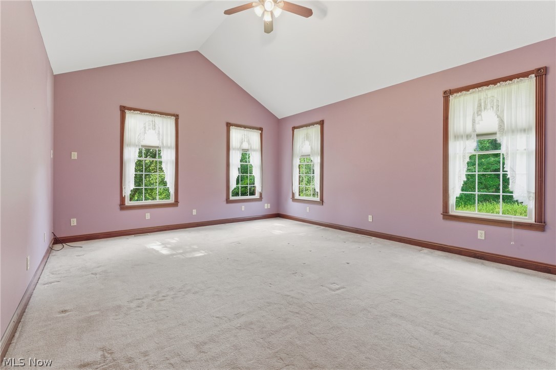 2184 Brenner Road Northeast Carrollton, OH 44615 - Photo 16 of 50 Spacious room featuring a vaulted ceiling with a ceiling fan, light purple walls, and five windows with white sheer curtains