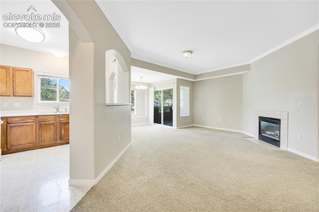 3864 Riviera Grove, Unit 102 Colorado Springs, CO 80922 - Photo 3 of 24 Open-concept living space featuring a fireplace with white tile surround, crown molding, and neutral carpeting
