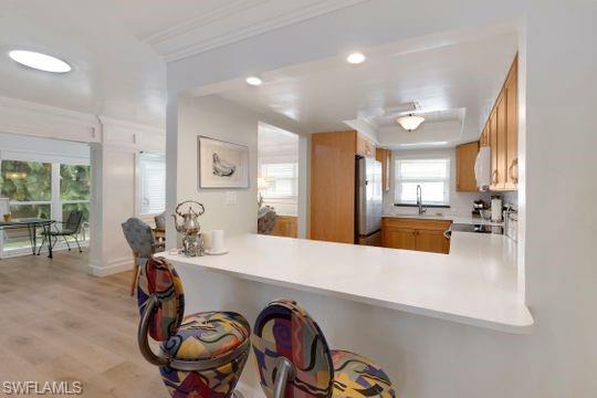 265 Yorkshire Court, Unit 8 Naples, FL 34112 - Photo 26 of 33 Kitchen featuring light countertops, light wood-type flooring, ornamental molding, freestanding refrigerator, and a breakfast bar