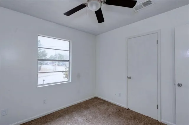 an empty room with ceiling fan and windows