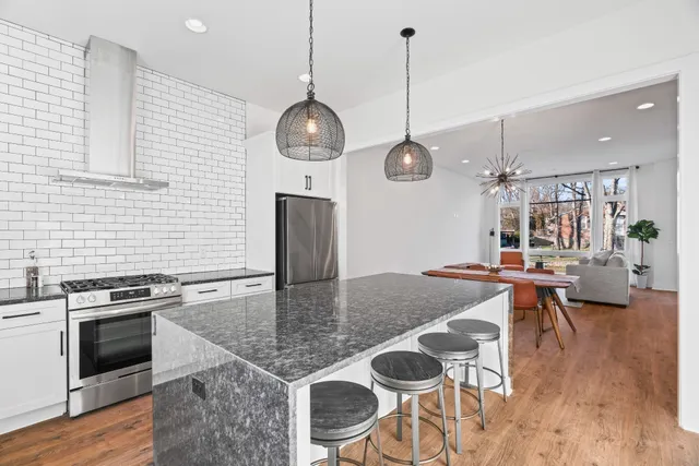 a kitchen with stainless steel appliances granite countertop a stove a refrigerator a oven a sink a dining table and chairs with wooden floor