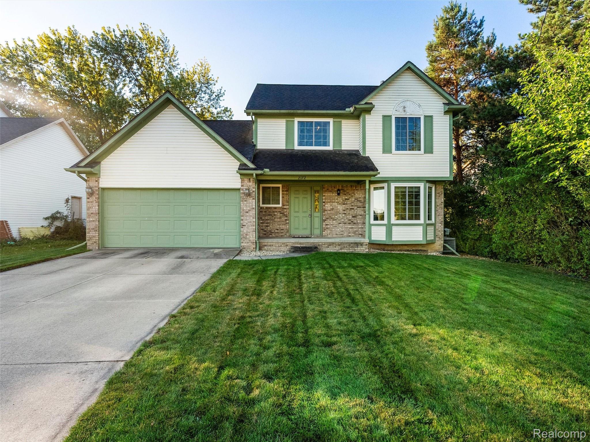 Traditional home with driveway, a front lawn, brick siding, an attached garage, and a porch